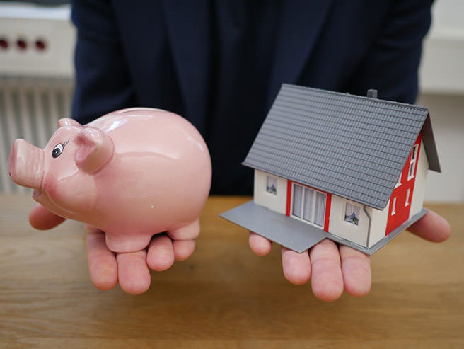 Man holding a pink piggy bank in one hand and a model house in the other