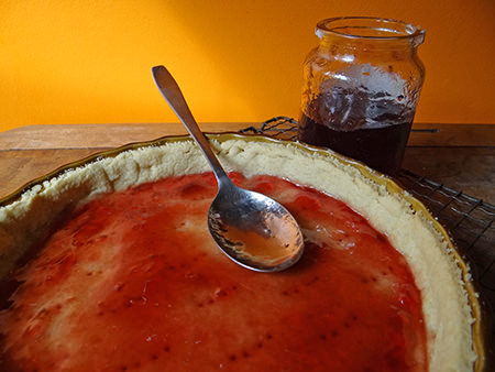 Raspberry jelly spread on a cooked Bakewell tart shortcrust pastry base