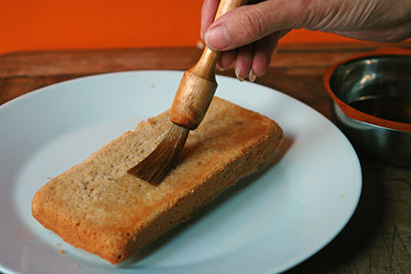 brushing rum syrup on a layer of chocolate caramel chestnut cake