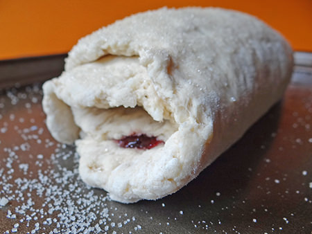Rolled up jam roly poly with top brushed with milk and sprinkled with granulated sugar
