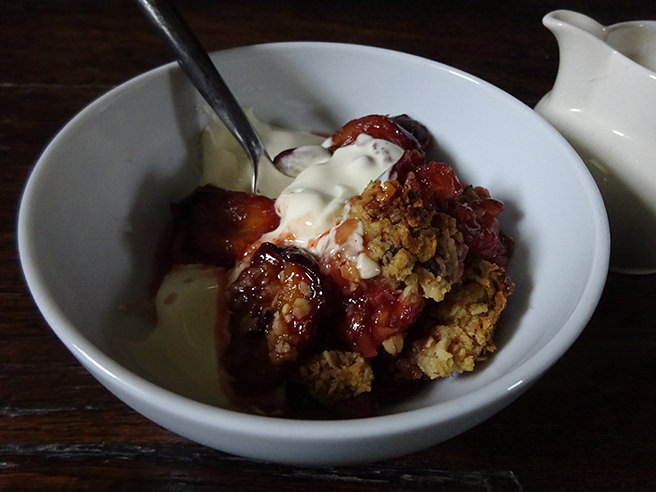 Bowl of spiced plum crumble with thick double cream