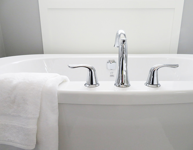 White bathtub with stainless steel taps and white towel thrown over