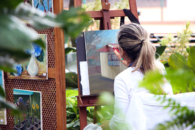 Woman painting a canvas surrounded by plants