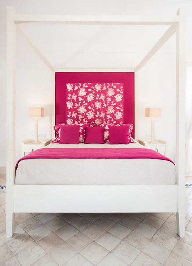 White painted four poster bed with hibiscus pink headboard, cushions and blanket