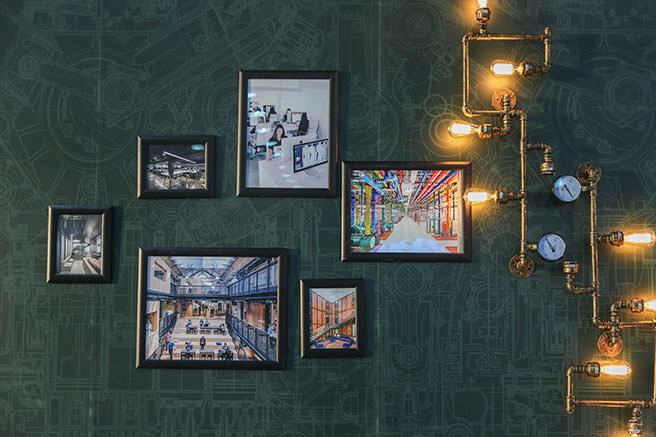 Artworks hung on a green wallpapered background illuminated by industrial style lighting